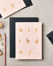 Pink birthday card with gold text on a gray surface