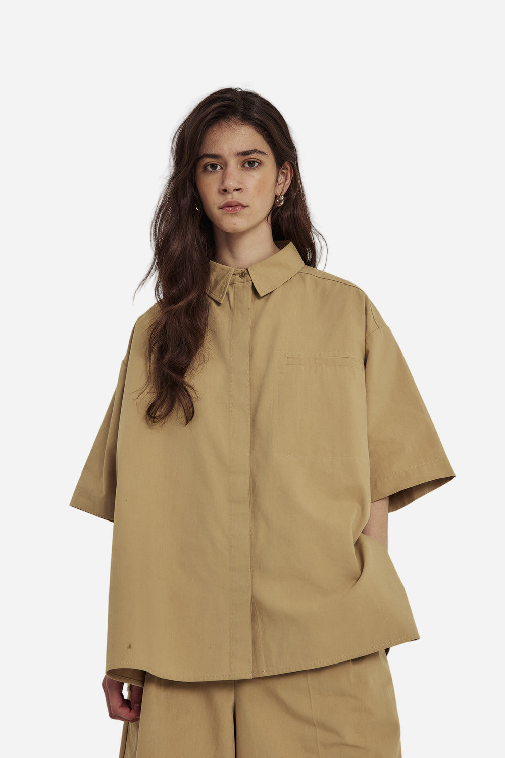 Woman wearing a beige shirt and pants against a plain background