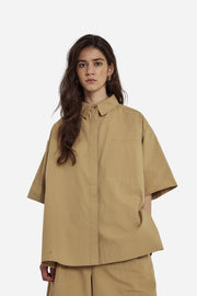 Woman wearing a beige shirt and pants against a plain background