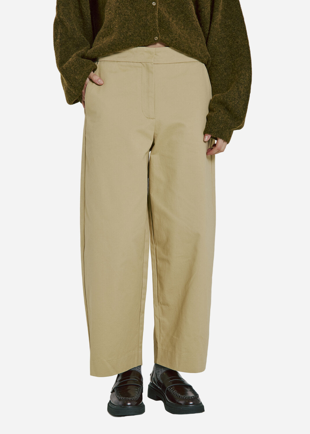 Person wearing beige pants and a green sweater on a plain background