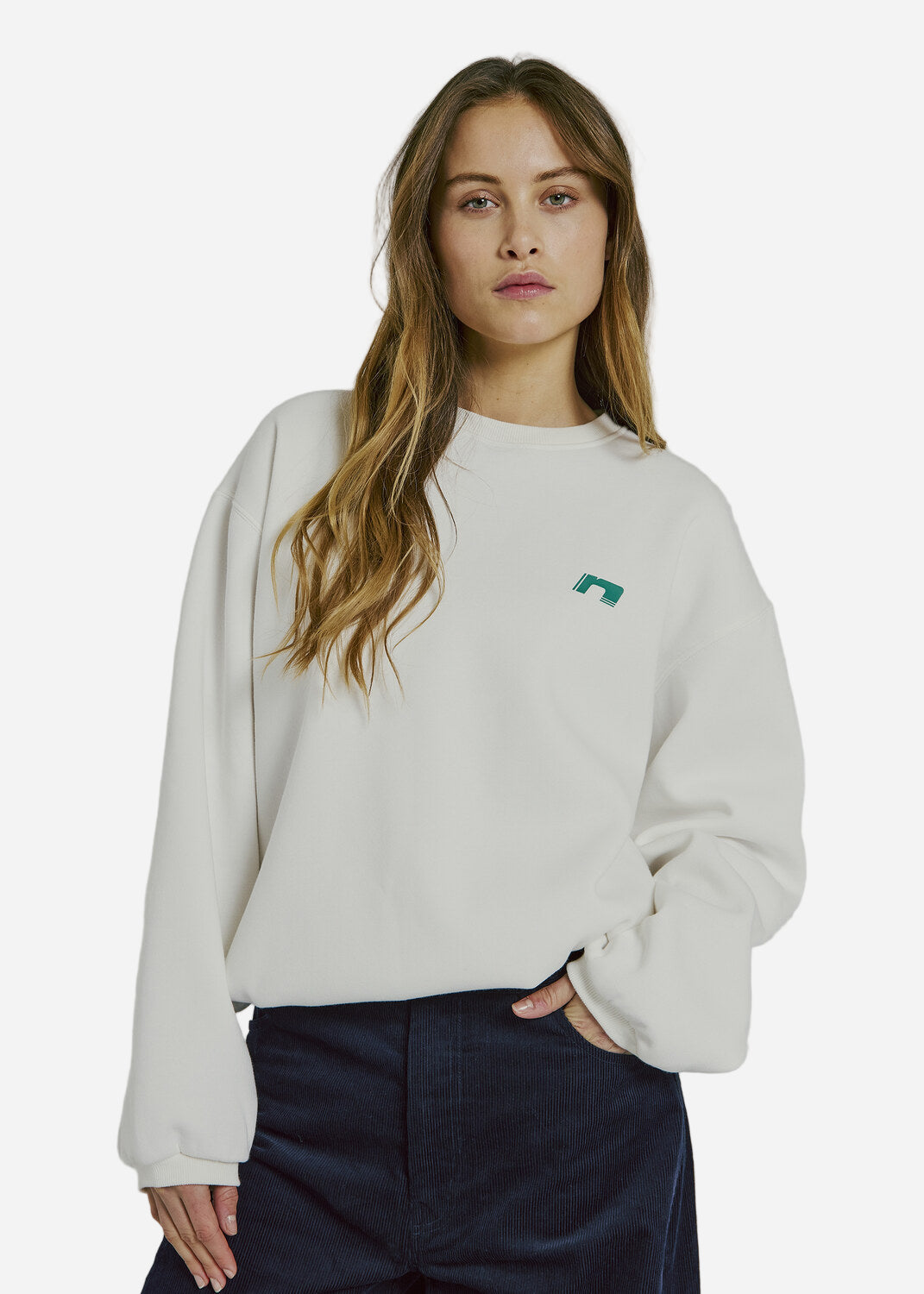 Woman wearing a white sweatshirt with a small green logo on a plain background