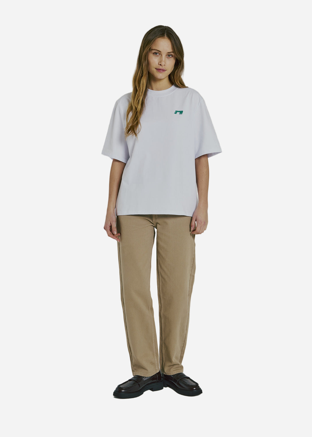 Woman wearing a white t-shirt with a logo and beige pants on a plain background