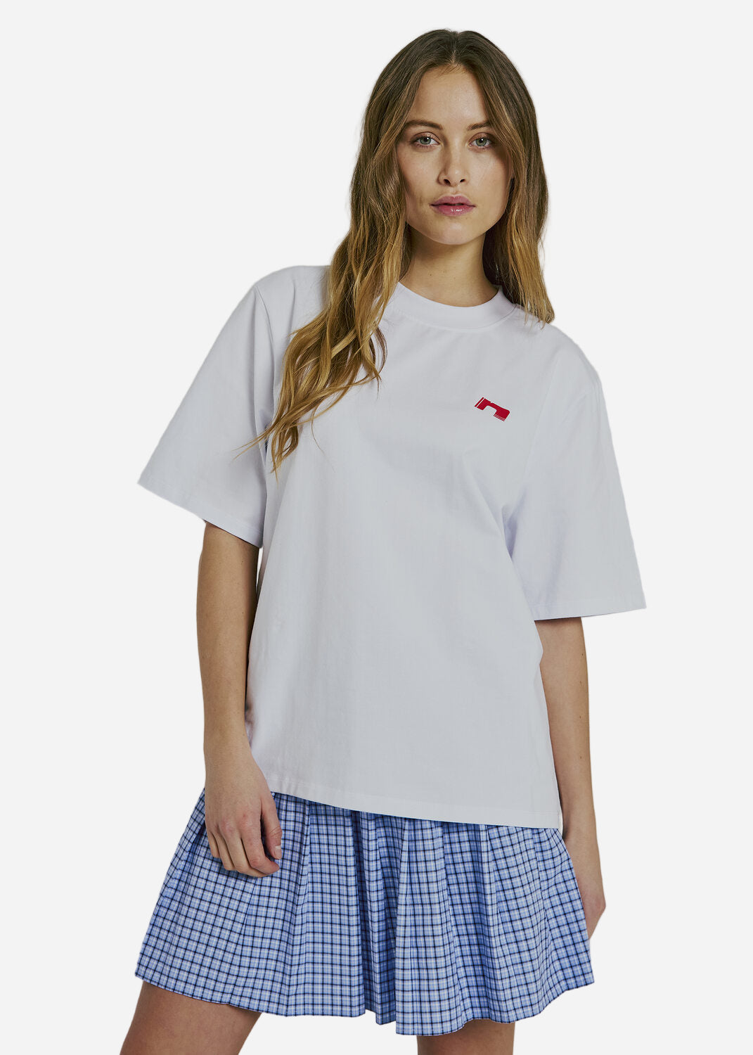 Woman wearing a white t-shirt with a red logo and a blue checkered skirt on a plain background