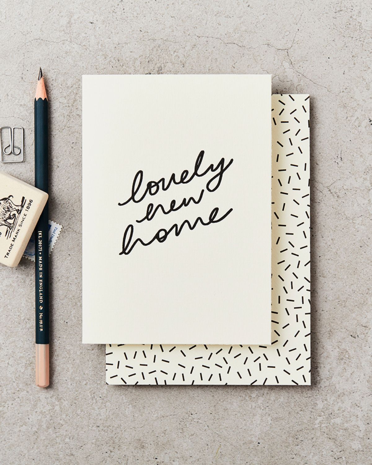 Greeting card with 'lovely new home' text on a concrete surface with a pencil and rubber.