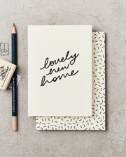 Greeting card with 'lovely new home' text on a concrete surface with a pencil and rubber.