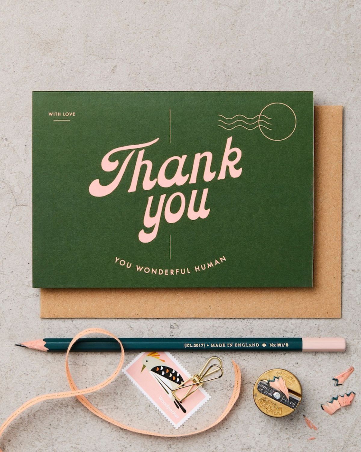 Green card with 'Thank you' text, brown envelope, pencil, and decorative items on a gray surface