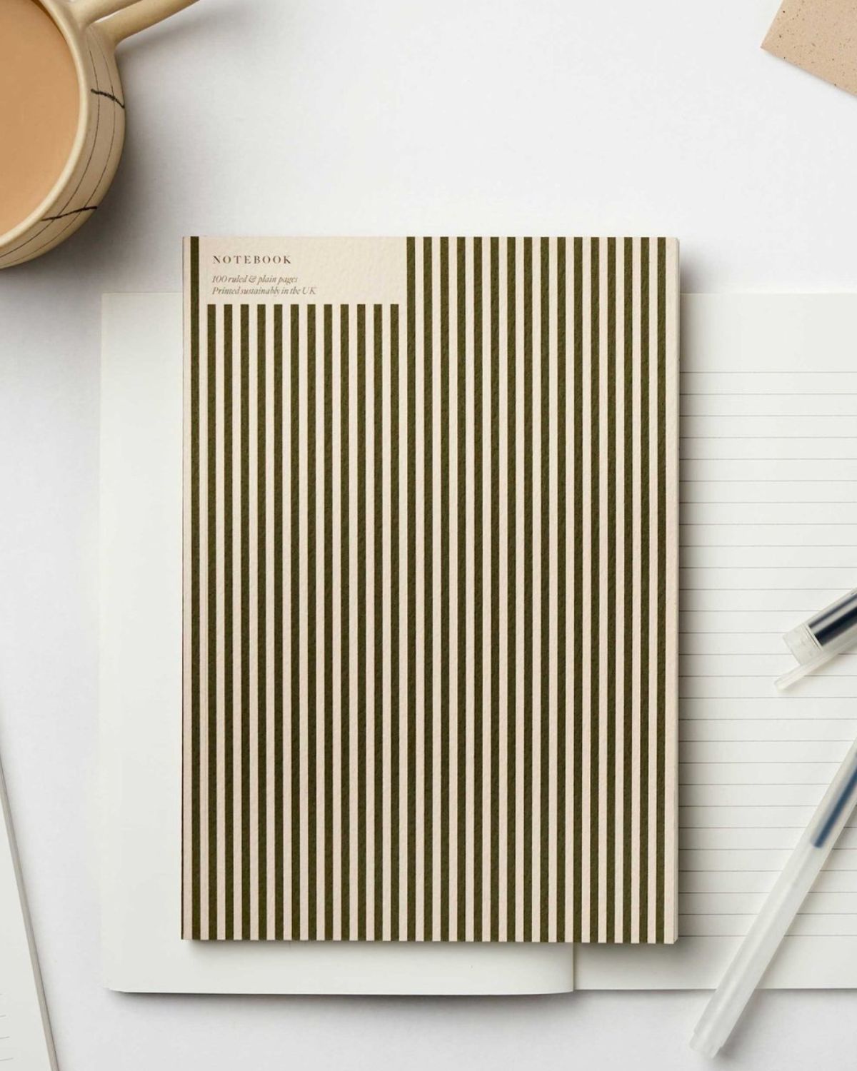 Notebook with striped cover on a white surface with a pen and cup of coffee.