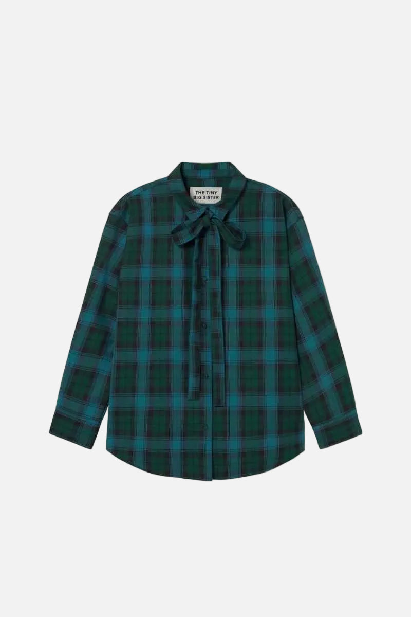 A long-sleeve plaid button-up shirt with a tie-neck bow, featuring a dark green and teal tartan pattern, laid flat against a light off-white background.