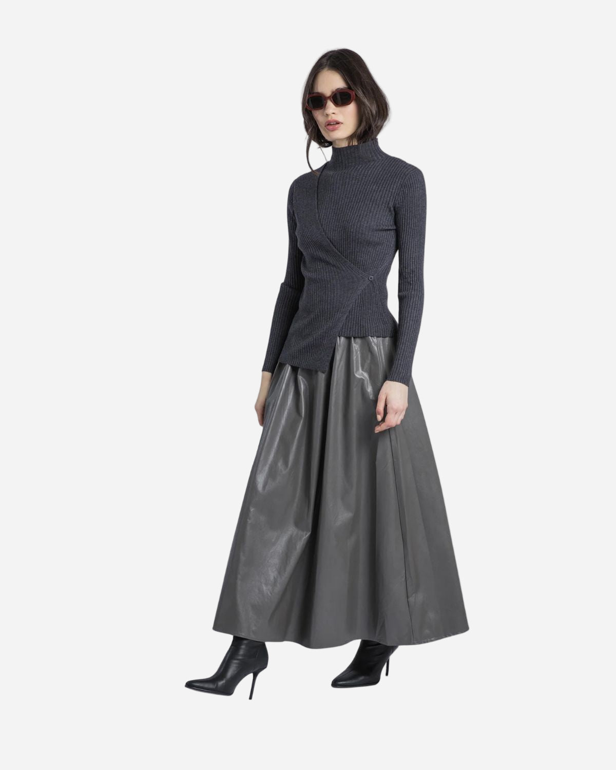 Woman wearing a dark grey turtleneck and long grey faux leather skirt on a white background