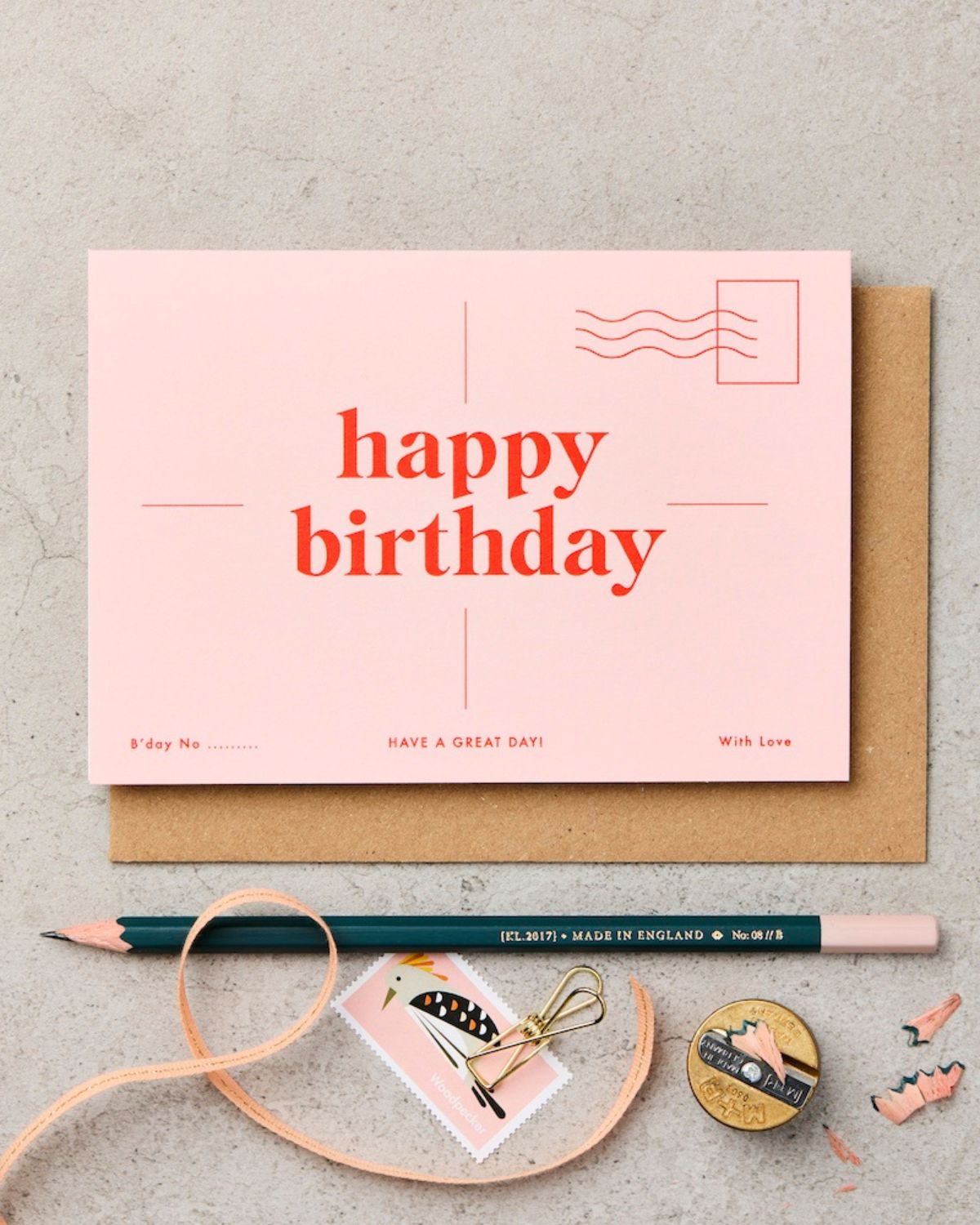 Pink birthday card with a pencil and decorative elements on a gray surface