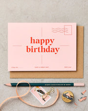 Pink birthday card with a pencil and decorative elements on a gray surface