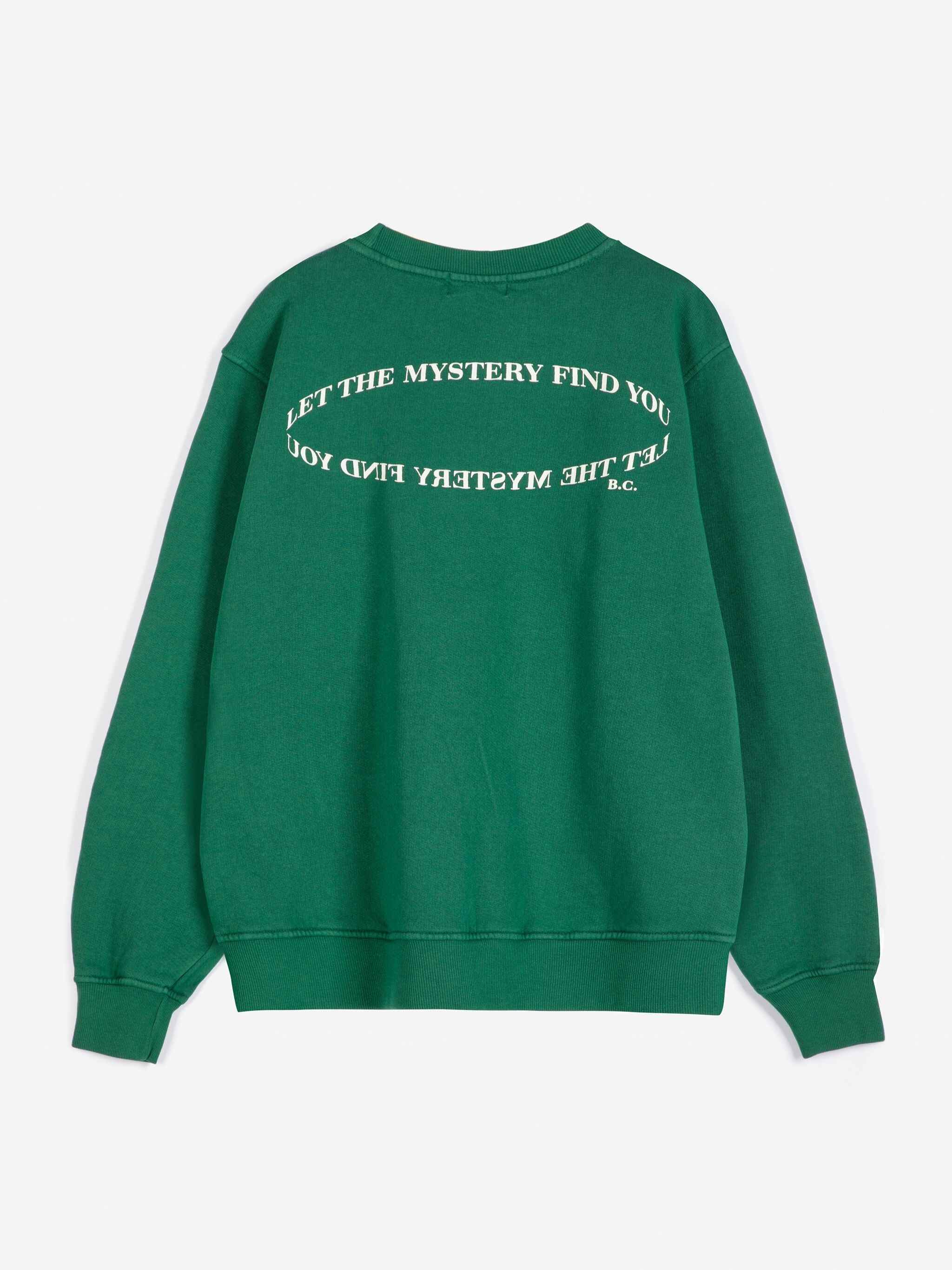 A green crewneck sweatshirt shown from the back, featuring white text that reads 'LET THE MYSTERY FIND YOU' in a circular design.