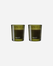 Two green glass candles with the Meraki brand logo, set against a white background.