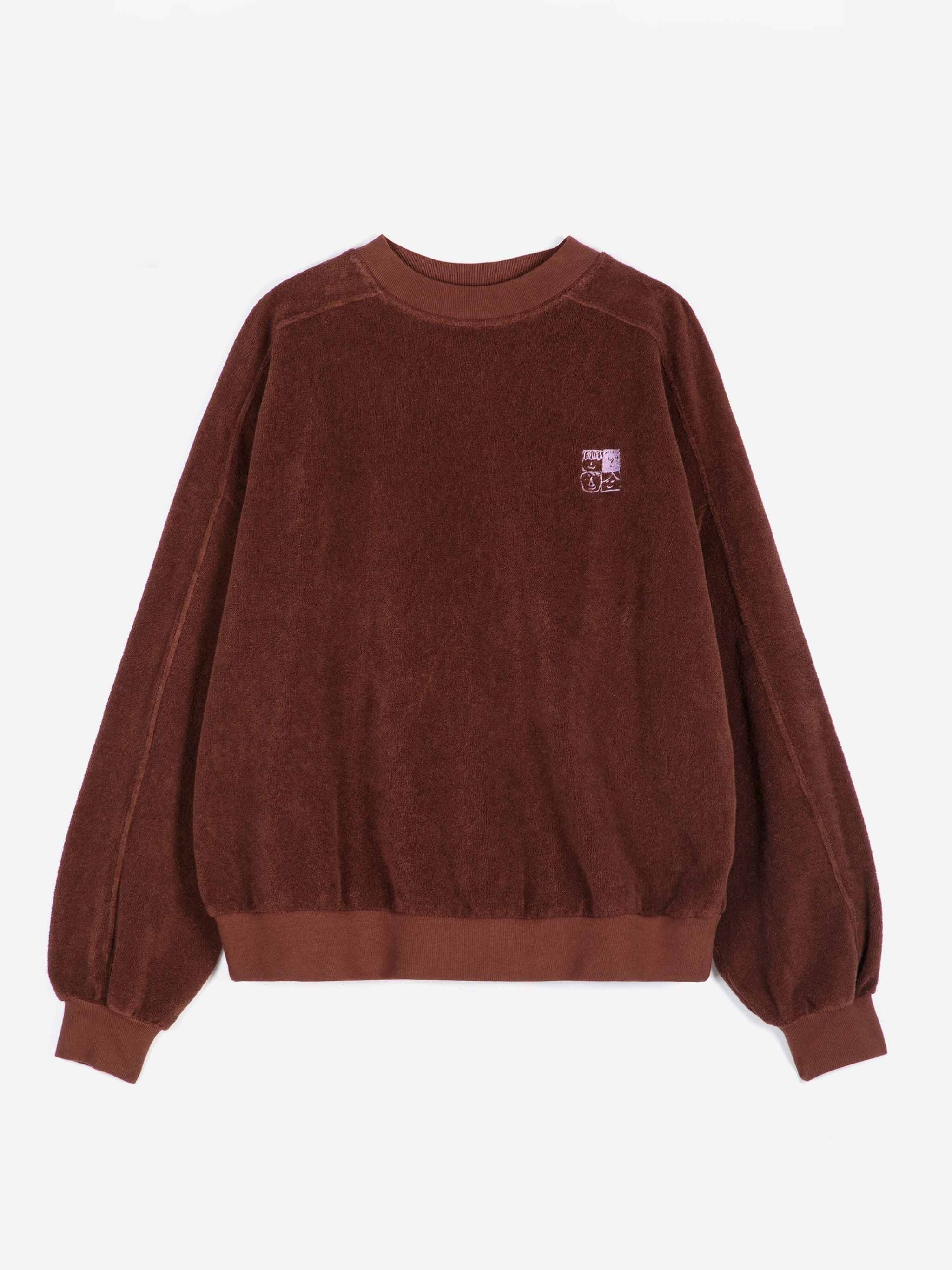 A dark brown long-sleeve crewneck sweatshirt with a small embroidered logo on the left chest, displayed flat against a light gray background.