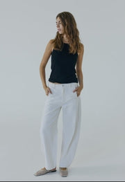 Woman wearing a black top and white pants against a plain background