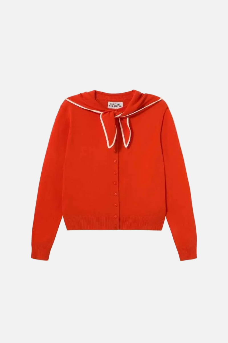 A bright red knit cardigan sweater with a white-trimmed sailor-style collar and a matching bow, shown flat against a light cream background.