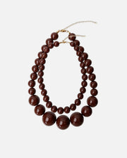 A multi-strand statement necklace featuring glossy dark brown spherical beads of varying sizes, accented by a delicate gold-tone chain extender, shown against a plain white background.
