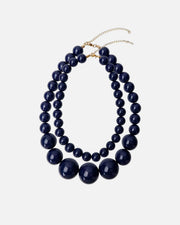 A double-strand statement necklace featuring glossy dark navy blue beads of varying sizes, with a gold-tone chain extender clasp, shown on a plain white background.