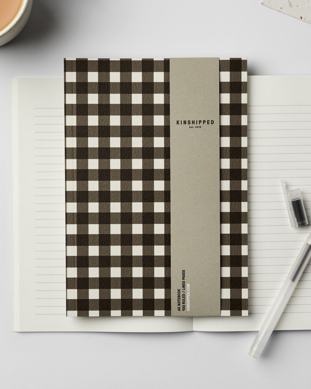 Notebook with gingham cover on a white surface with a pen and ink bottle.