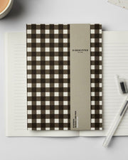 Notebook with gingham cover on a white surface with a pen and ink bottle.