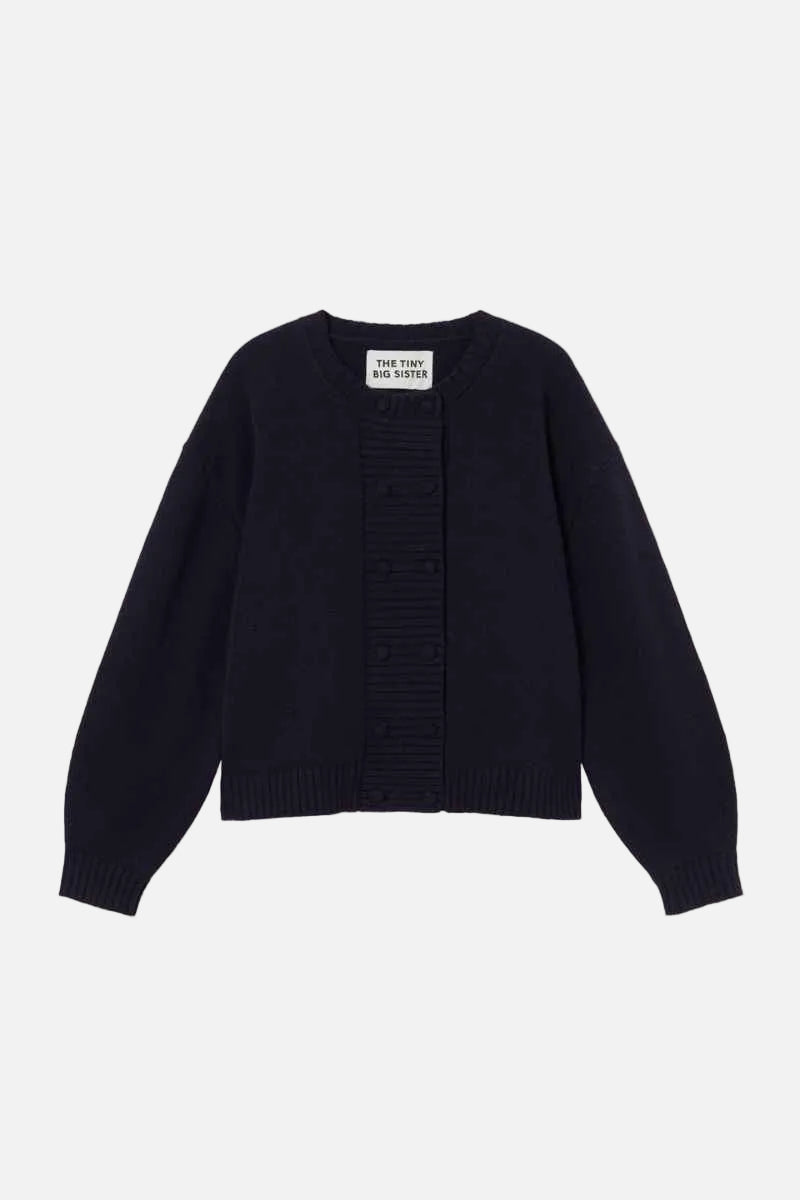 A dark navy blue knit cardigan sweater with a ribbed front panel and long sleeves, laid flat against a light cream background.  