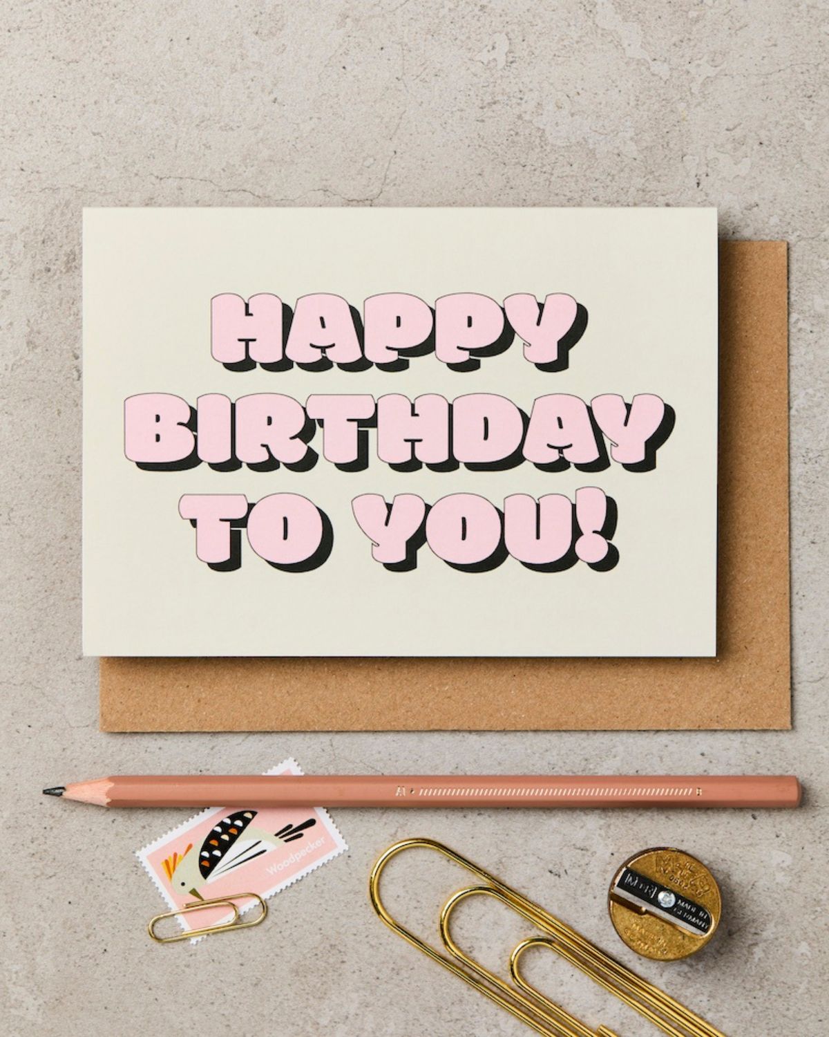 Birthday card with 'Happy Birthday to You!' text, pencil, paper clips, and stationery items on a textured surface.