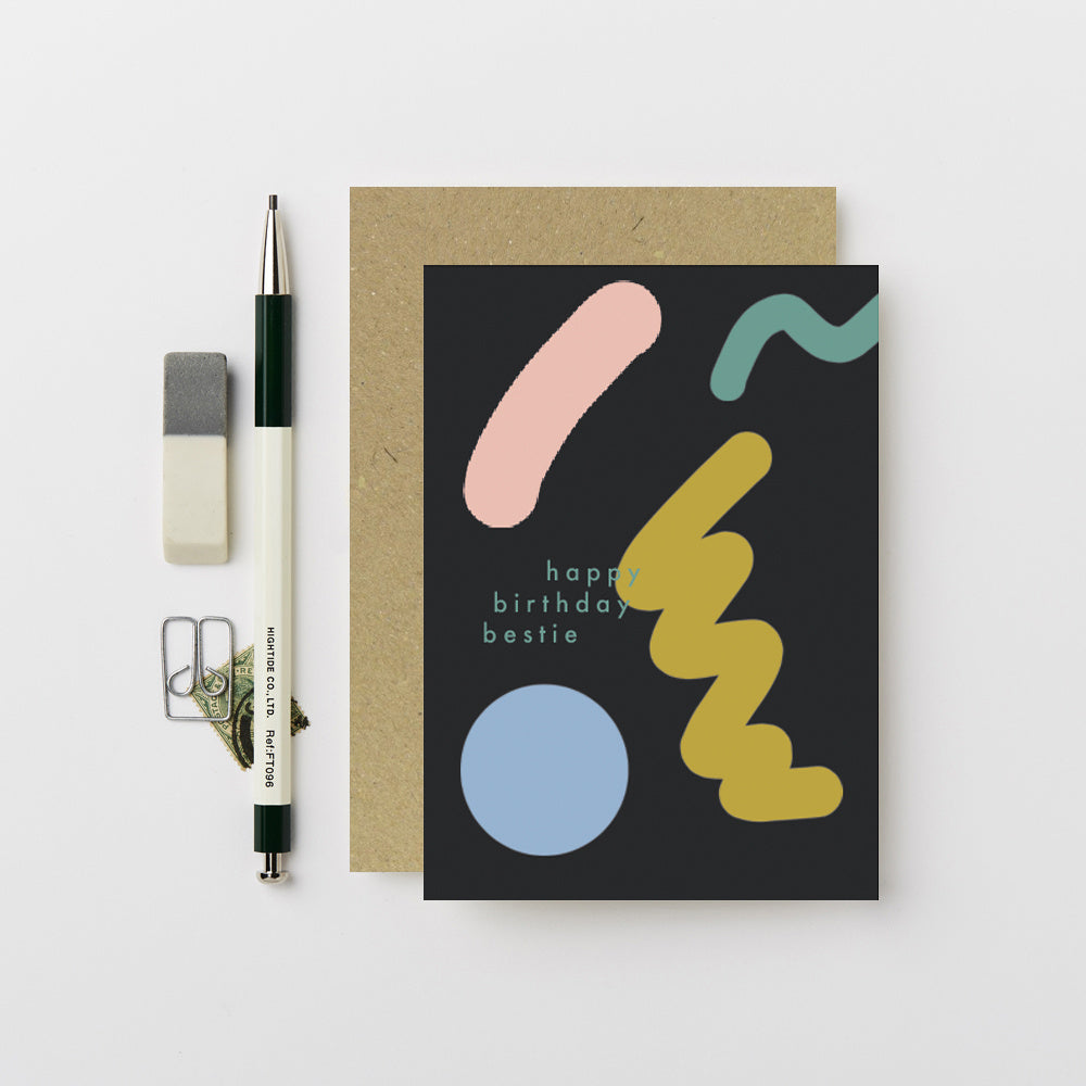 Greeting card with abstract designs and 'happy birthday bestie' text, placed on a white surface with stationery items.