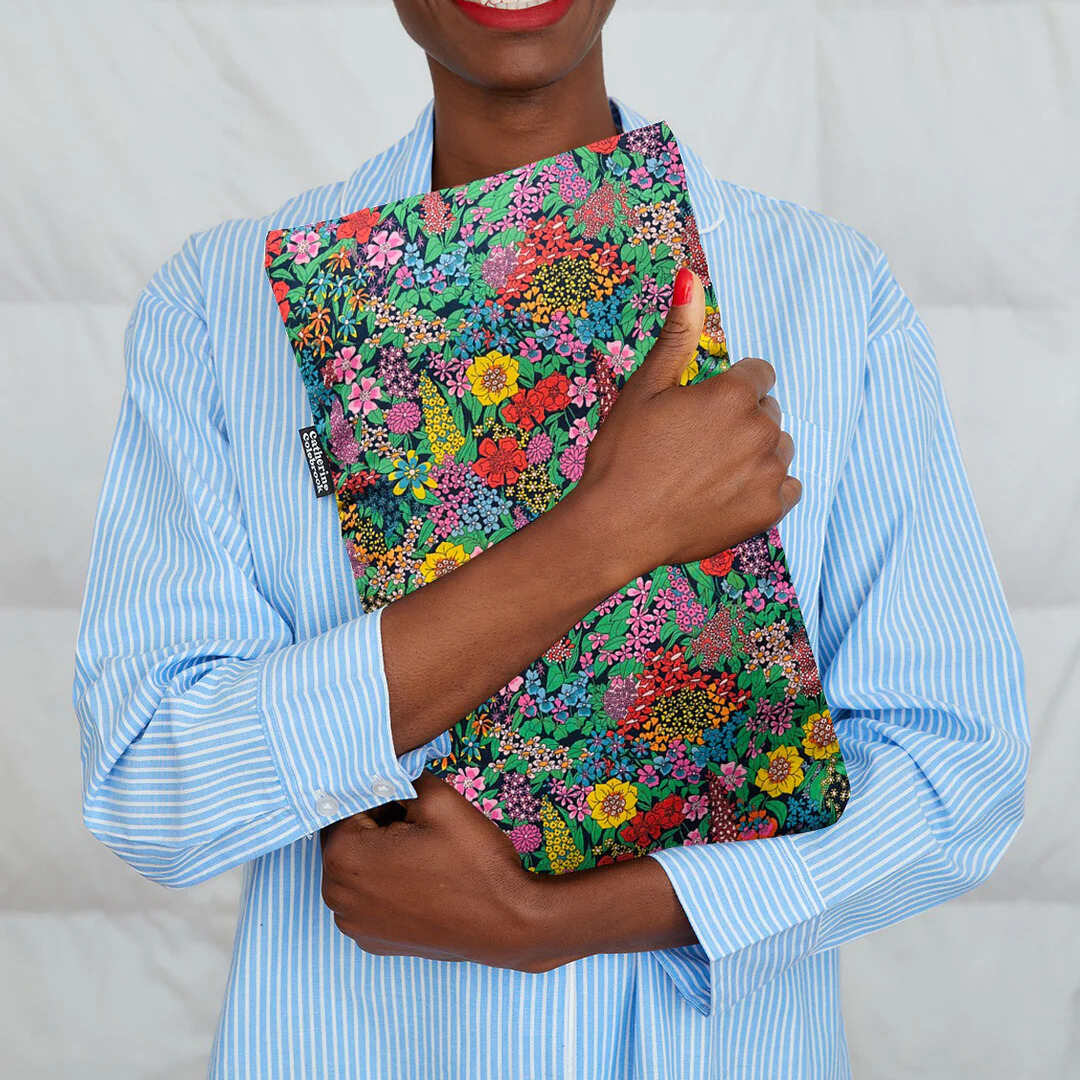 Person holding a colorful floral hot water bottle against a plain background