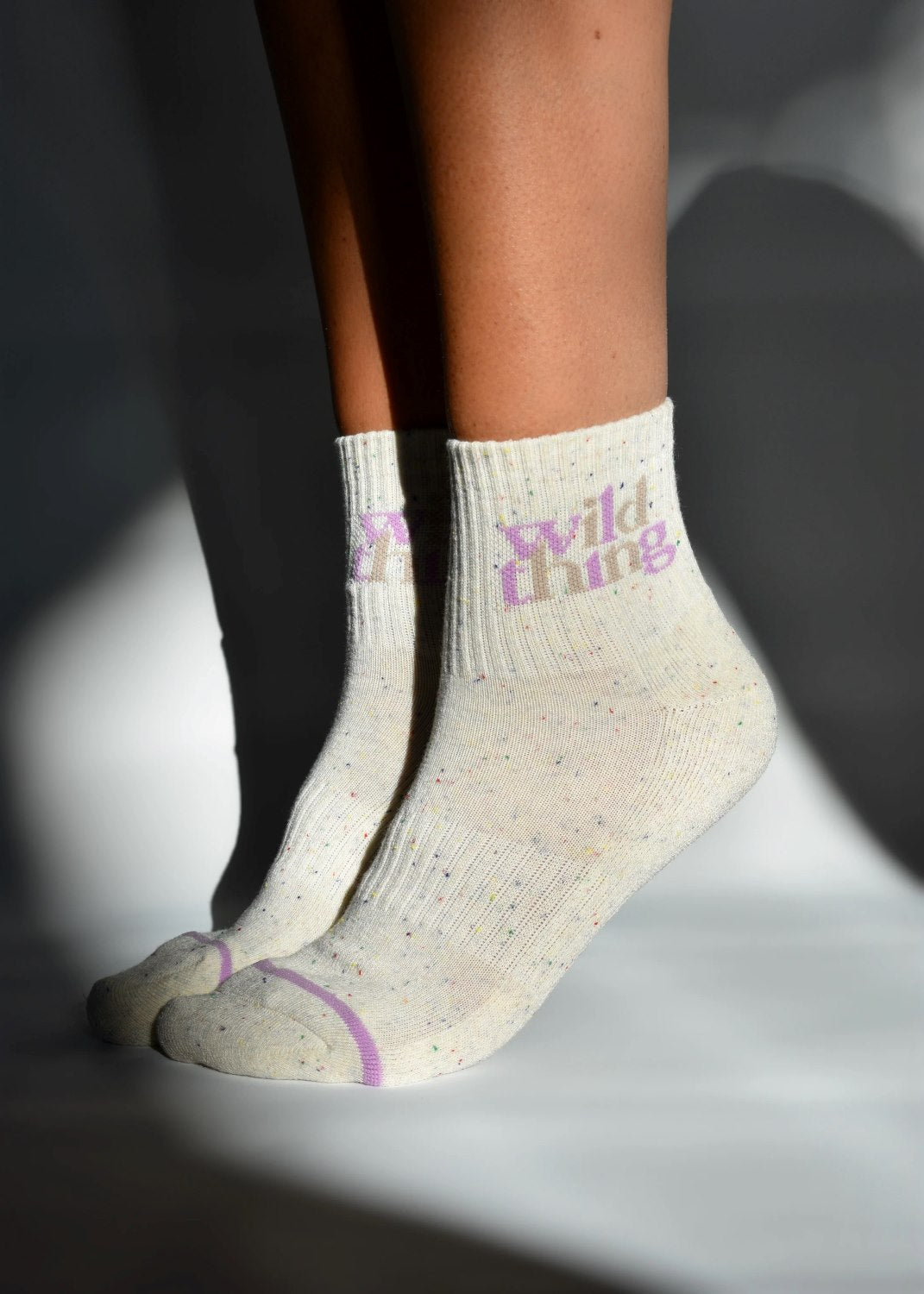 A pair of beige ribbed crew socks with 'WILD THING' text detail above the ankle, featuring a subtle confetti pattern and elasticated band.