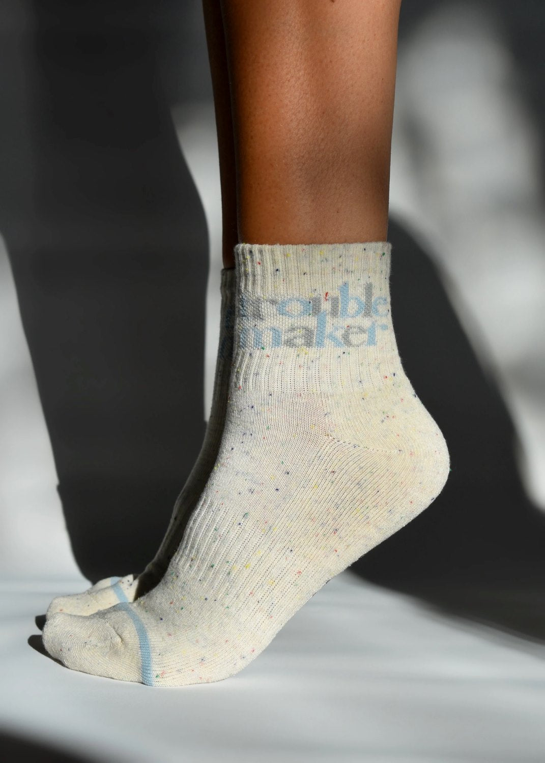 A pair of beige ribbed crew socks with 'TROUBLE MAKER' text detail, featuring a subtle confetti pattern and elasticated stretch.