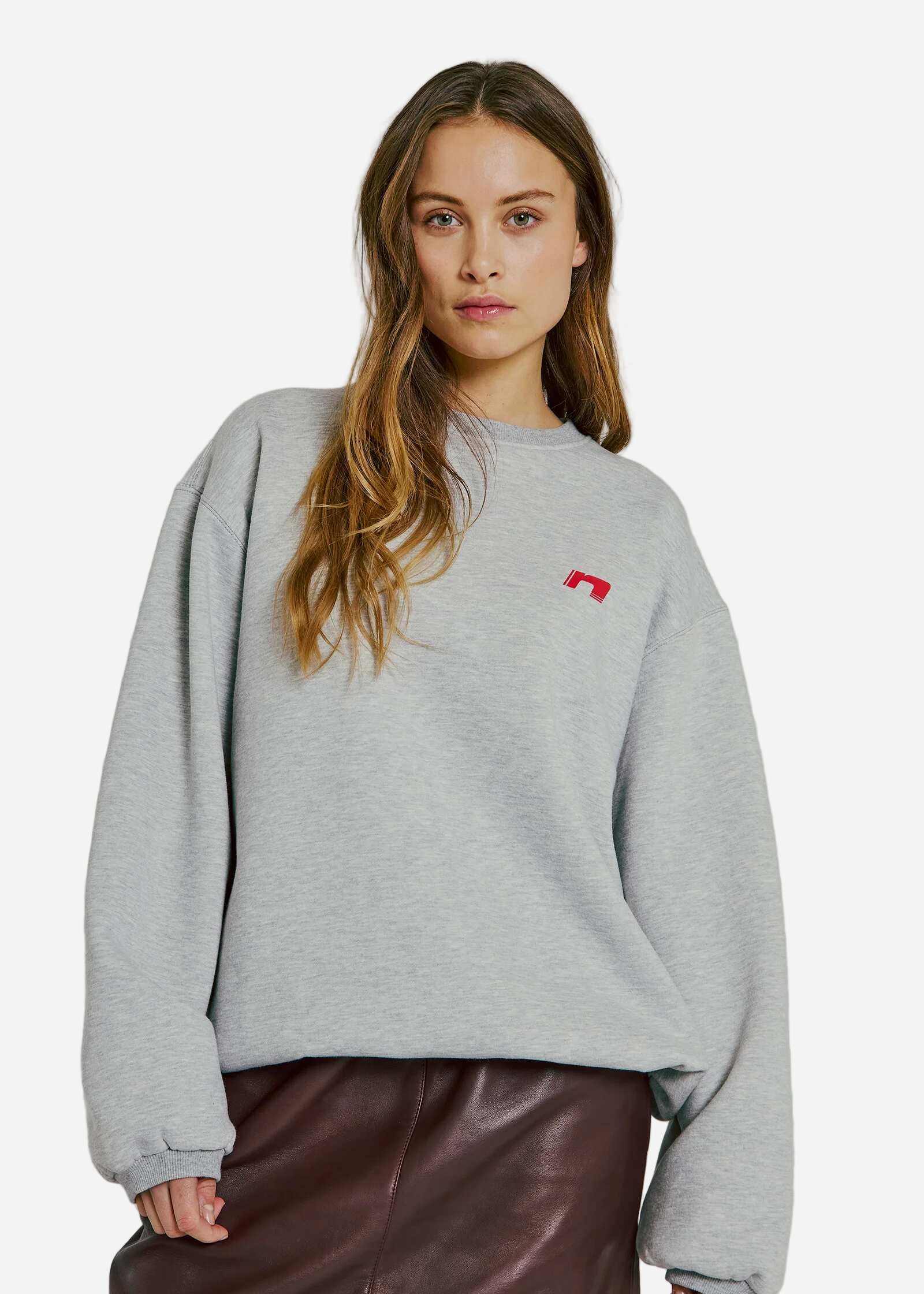 Person wearing a gray sweatshirt with a red logo on a plain background