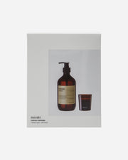 A gift box with a transparent bottle of hand soap and a dark wood candle, both with the brand 'meraki' visible on the label and packaging.