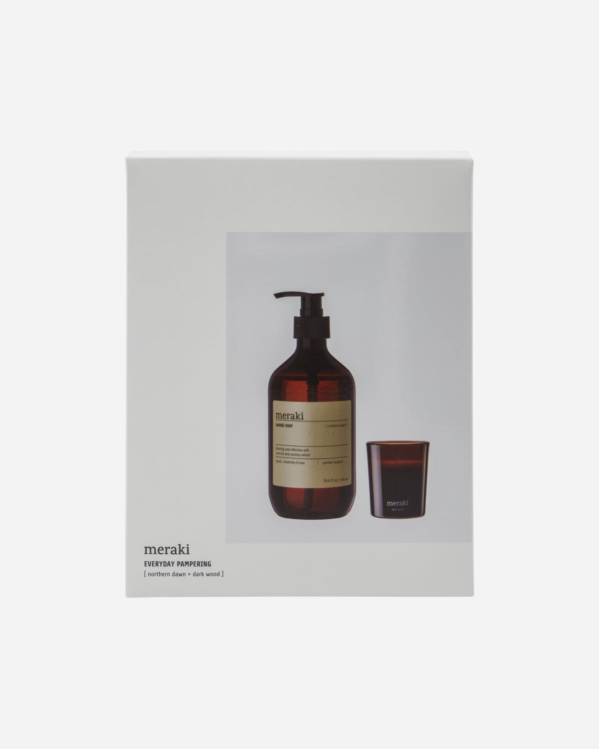 A gift box with a transparent bottle of hand soap and a dark wood candle, both with the brand 'meraki' visible on the label and packaging.