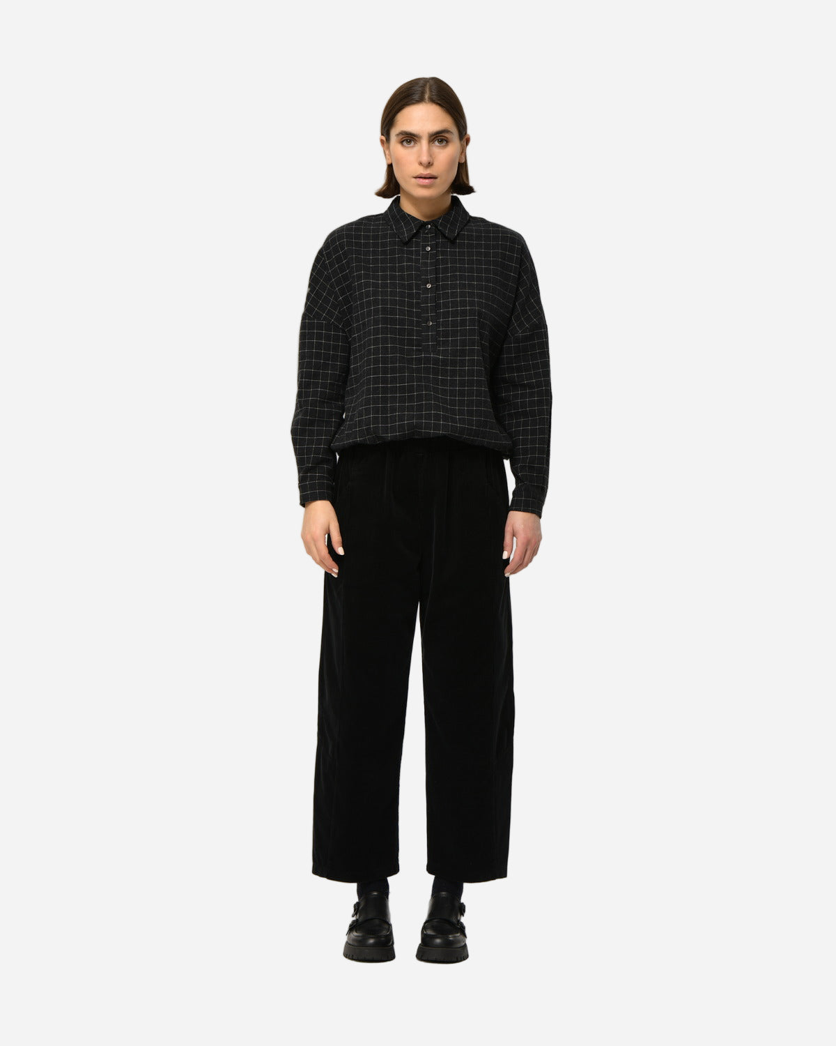 Person wearing a black checkered shirt and black pants on a white background