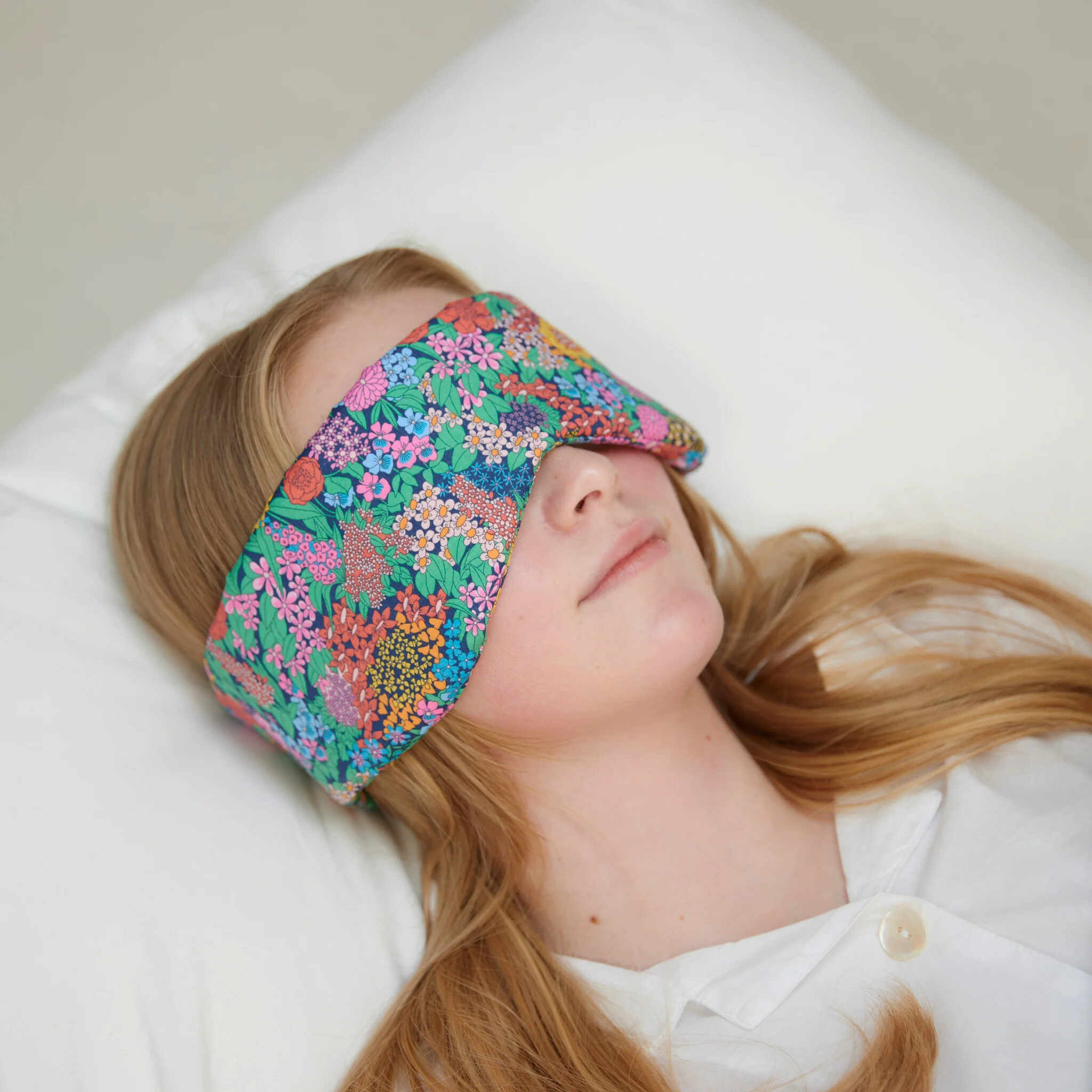 Person wearing a colorful floral sleep mask on a white pillow