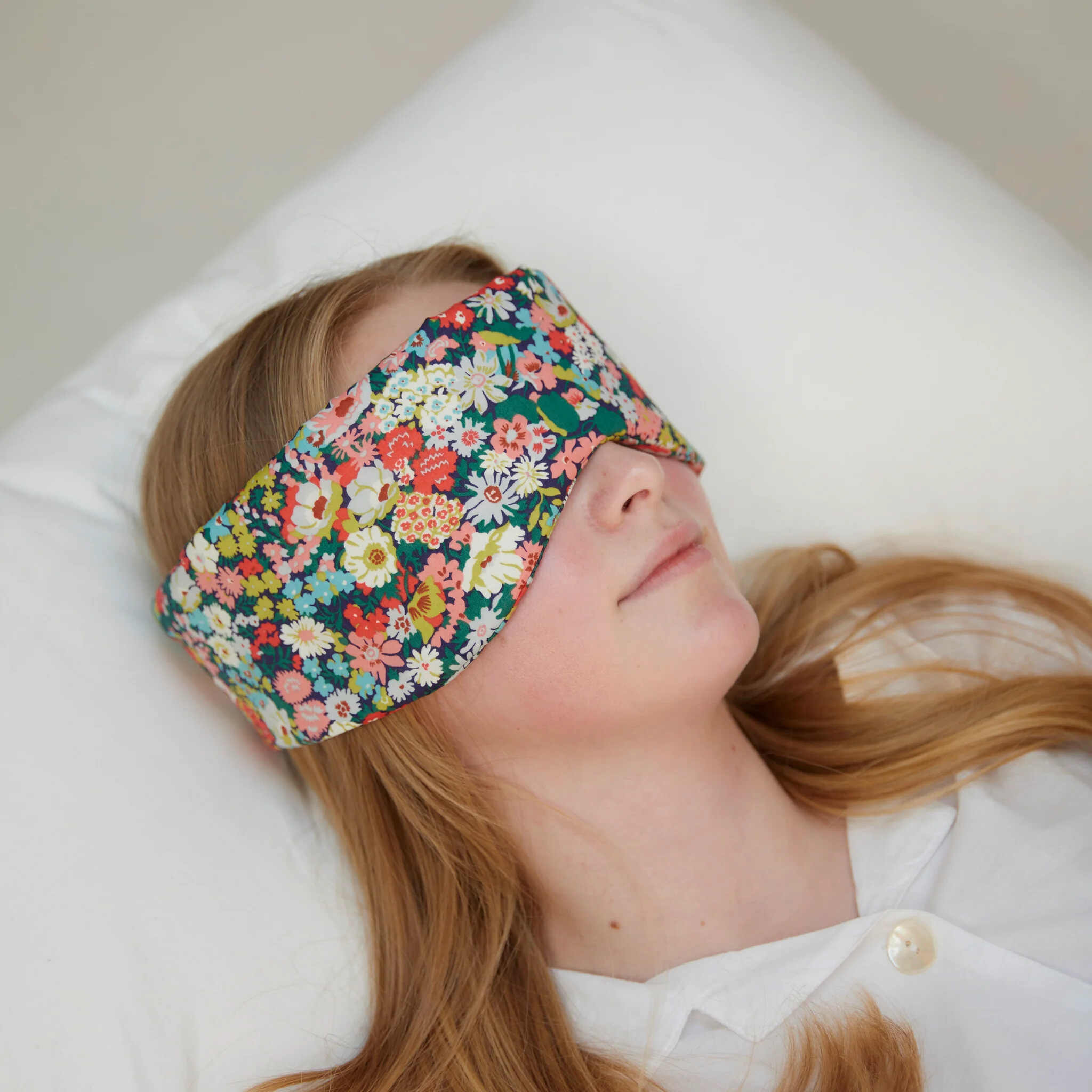 Person wearing a colorful floral sleep mask on a white pillow