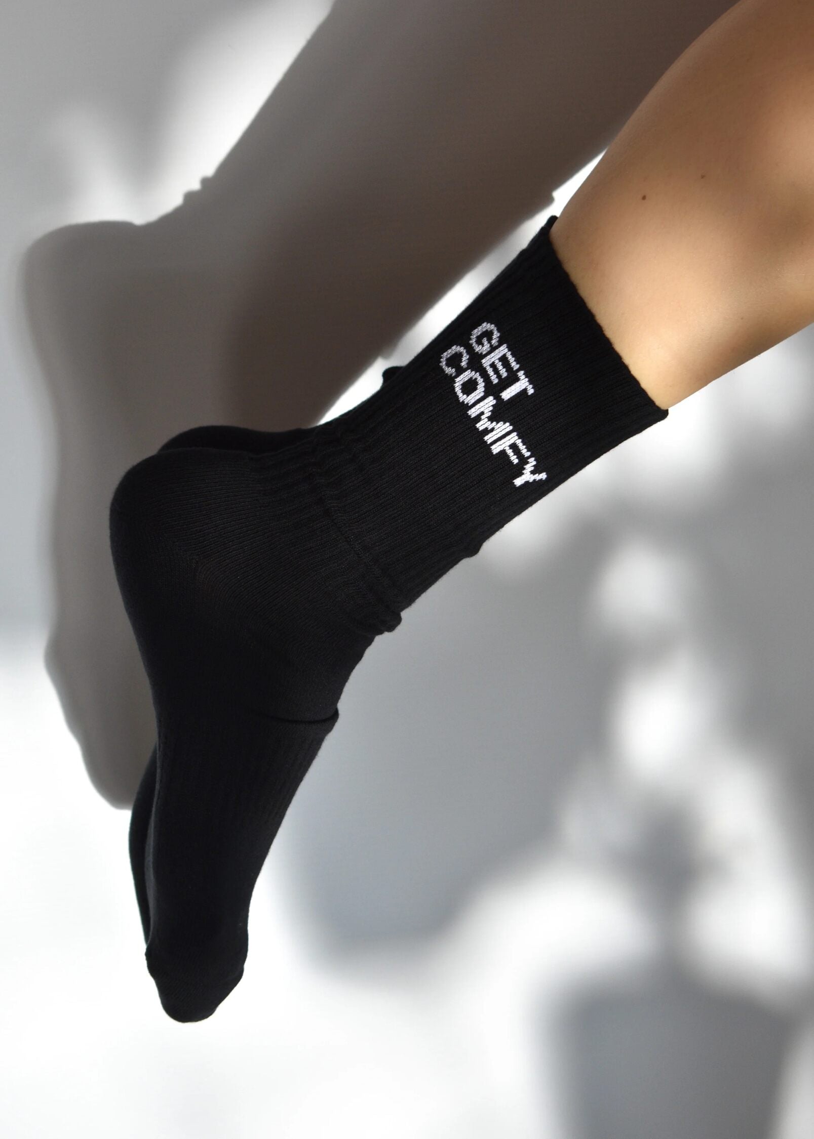 A black crew-length sock with 'GET COMFY' text on the side, featuring arch support and cushioned heel and toe areas.