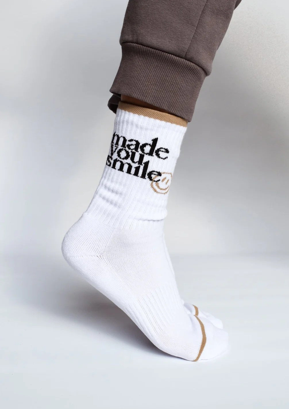 A white crew-length sock with the text 'MADE YOU SMILE' and a smiley face design in black, positioned on a person's leg.