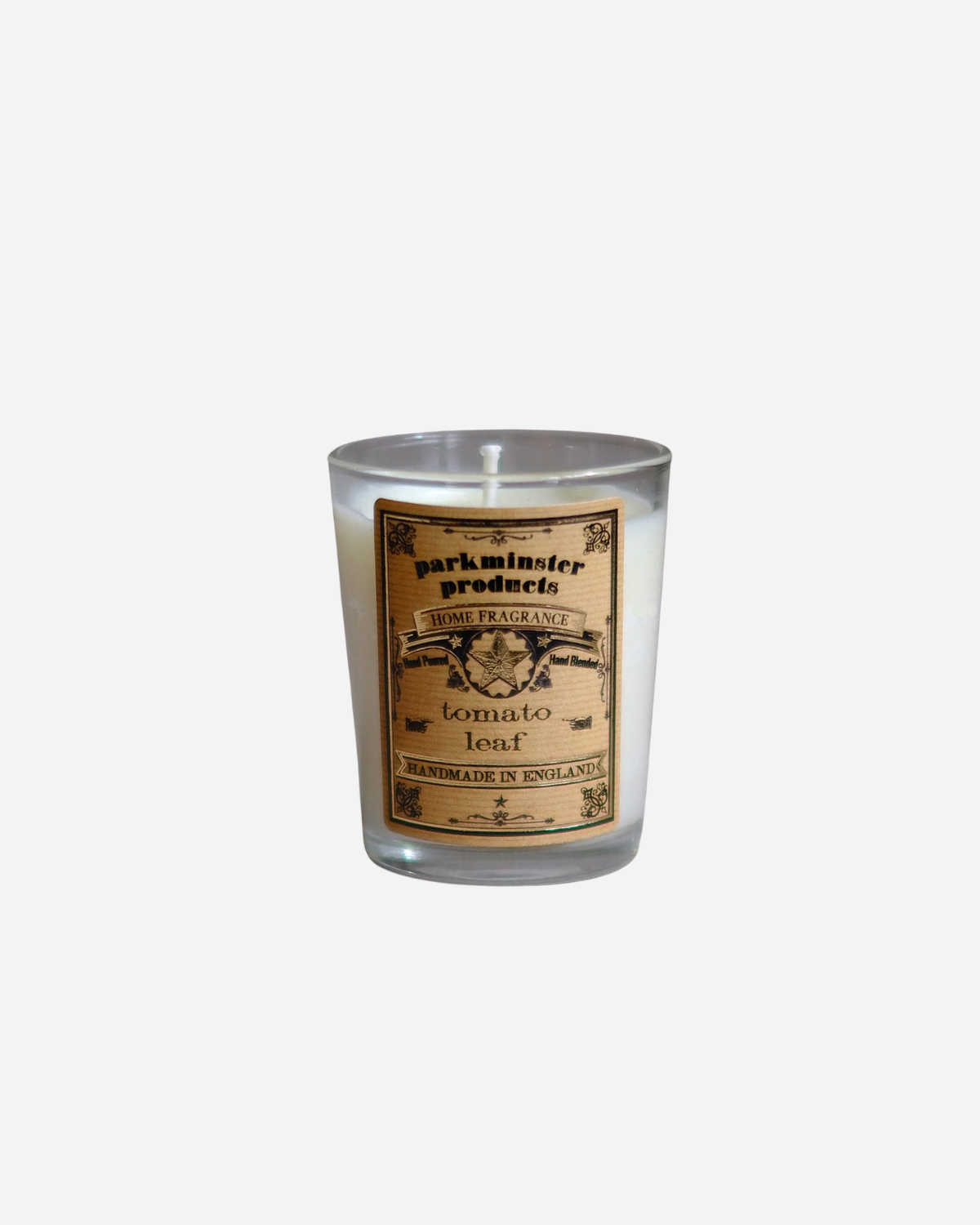 A clear glass mini votive candle with a label that reads 'Tomato Leaf' and other text, indicating the fragrance of the candle.
