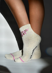 A pair of beige ribbed crew socks with 'LOVER GIRL' text in pink above the ankle, featuring a subtle confetti pattern and elasticated stretch.