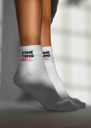 A pair of white ribbed crew socks with 'SOMETHING CUTE' text detail, worn on the lower leg above the ankle.