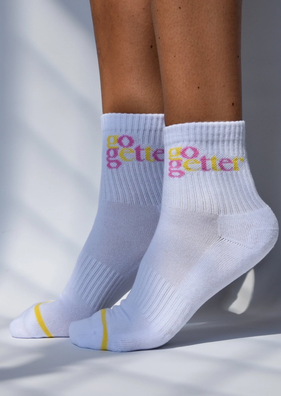 A pair of white ribbed crew socks with 'GO GETTER' text in multicolor above the ankle, featuring arch support and a cushioned heel and toe.